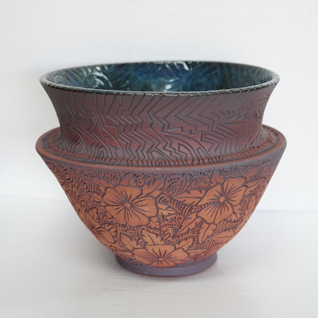 A ceramic bowl with a textured reddish-brown exterior featuring embossed floral patterns, and a glossy dark blue glazed interior, set against a plain white background.